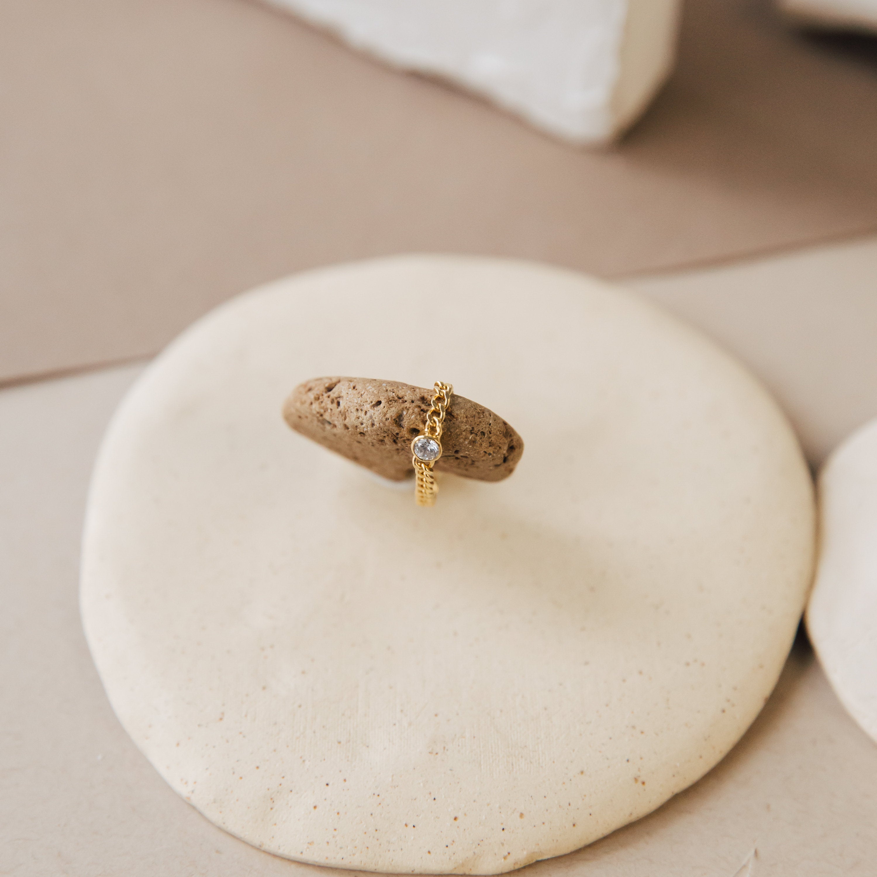 The Birthstone Curb Ring features a single personalized gemstone set atop a smooth, round beige surface.