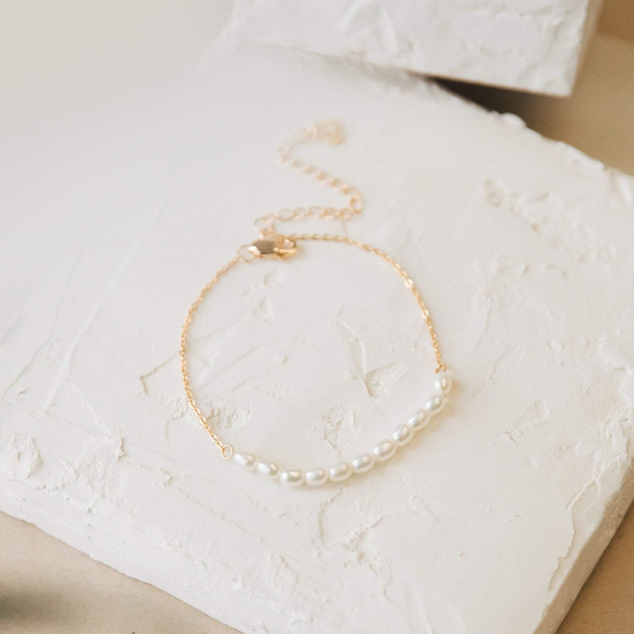 The Pearl Bead Bracelet features modern pearls on a gold chain and is shown on a textured white surface.