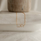 Pave Name Necklace with the name LUCY in sparkling personalized block letters, shown on a marble surface.