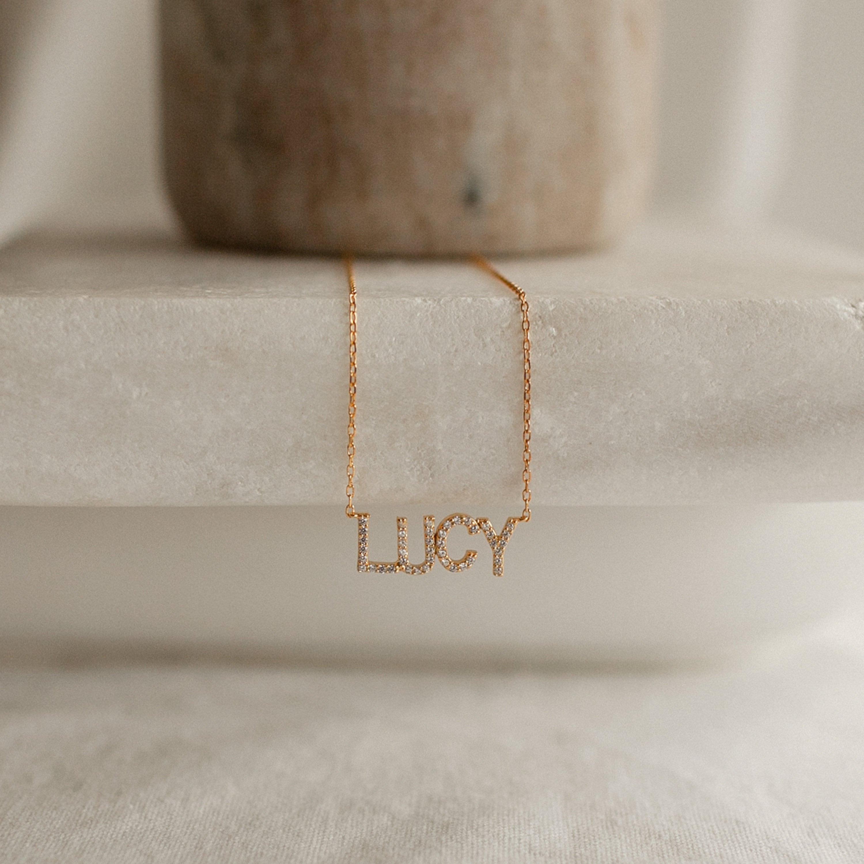 Pave Name Necklace with the name LUCY in sparkling personalized block letters, shown on a marble surface.