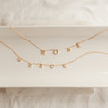 Two Pave Letter Necklaces in Rose Gold, featuring charms that spell ROSE and GRACE, are arranged on a white tray—an elegant way to personalize your style.