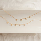 Two Pave Letter Necklaces in Rose Gold, featuring charms that spell ROSE and GRACE, are arranged on a white tray—an elegant way to personalize your style.