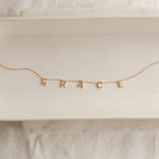The Pave Letter Necklace features dangling letter charms spelling GRACE, shown on a white ceramic tray—a meaningful necklace and an ideal choice for personalized jewelry.