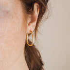 Close-up of a woman's ear wearing Anine Oval Hoops, showcasing the gold earrings against her brown hair and freckles.