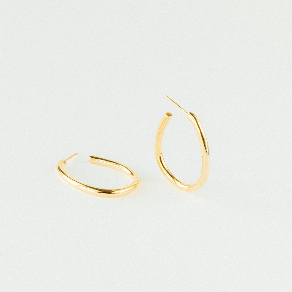 A pair of Anine Oval Hoops is displayed in gold against a plain white background.
