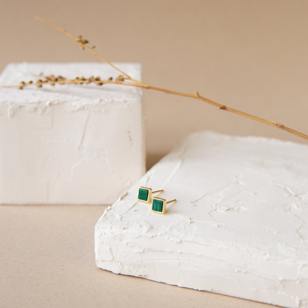 Malachite Studs: Gold geometric box-shaped earrings featuring green malachite, shown on textured white blocks with a dried twig.