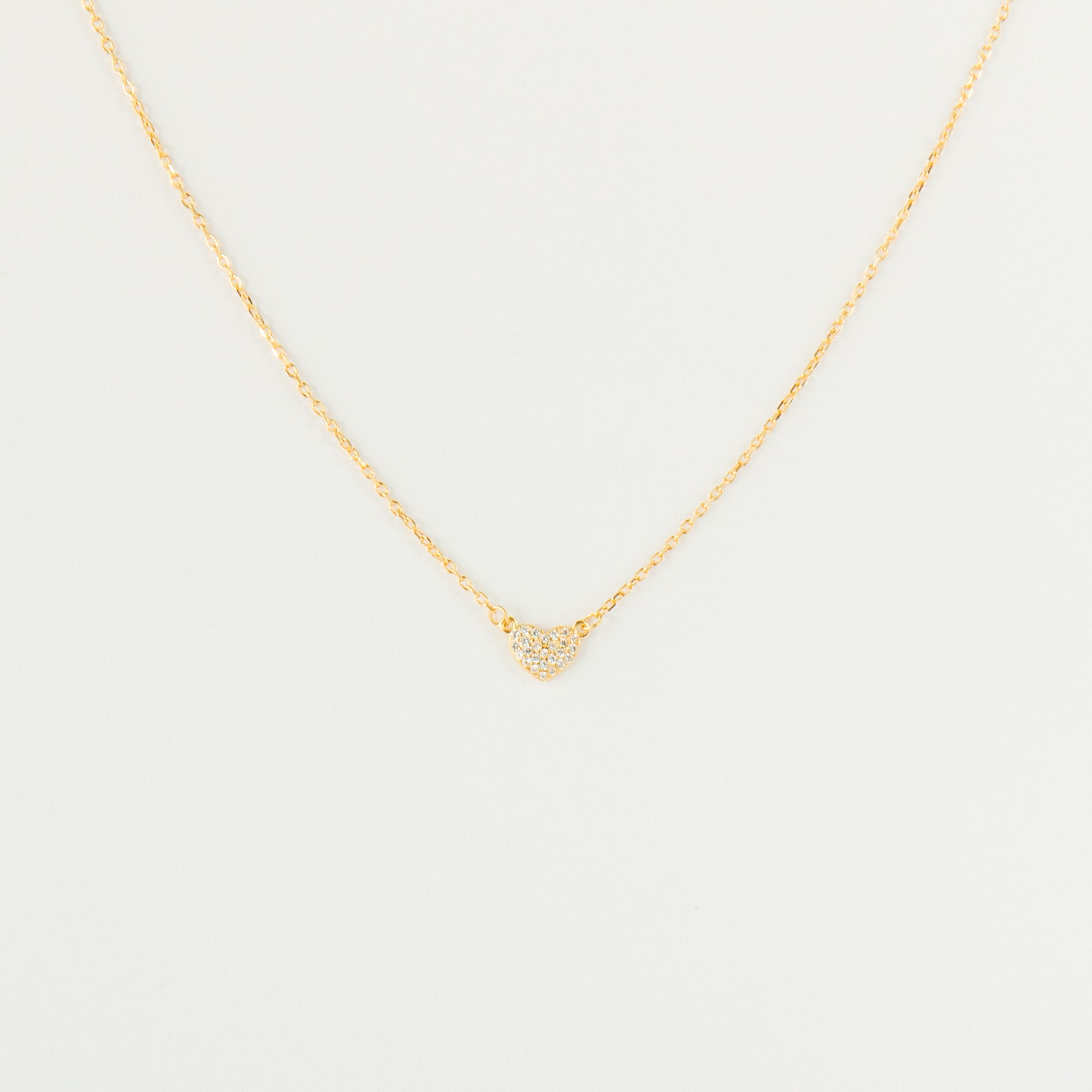 The Pave Heart Necklace features a gold chain with a minimalist heart pendant adorned with tiny clear stones—a delicate accessory perfect for everyday elegance.