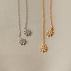 Pair these star-shaped pendant necklaces—one silver, one gold—displayed on a textured beige surface with our Lux Threader Earrings for an elegant look.