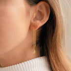 Close-up of a woman wearing Lux Threader Earrings—long gold threaders featuring a delicate star charm—set against a neutral background.