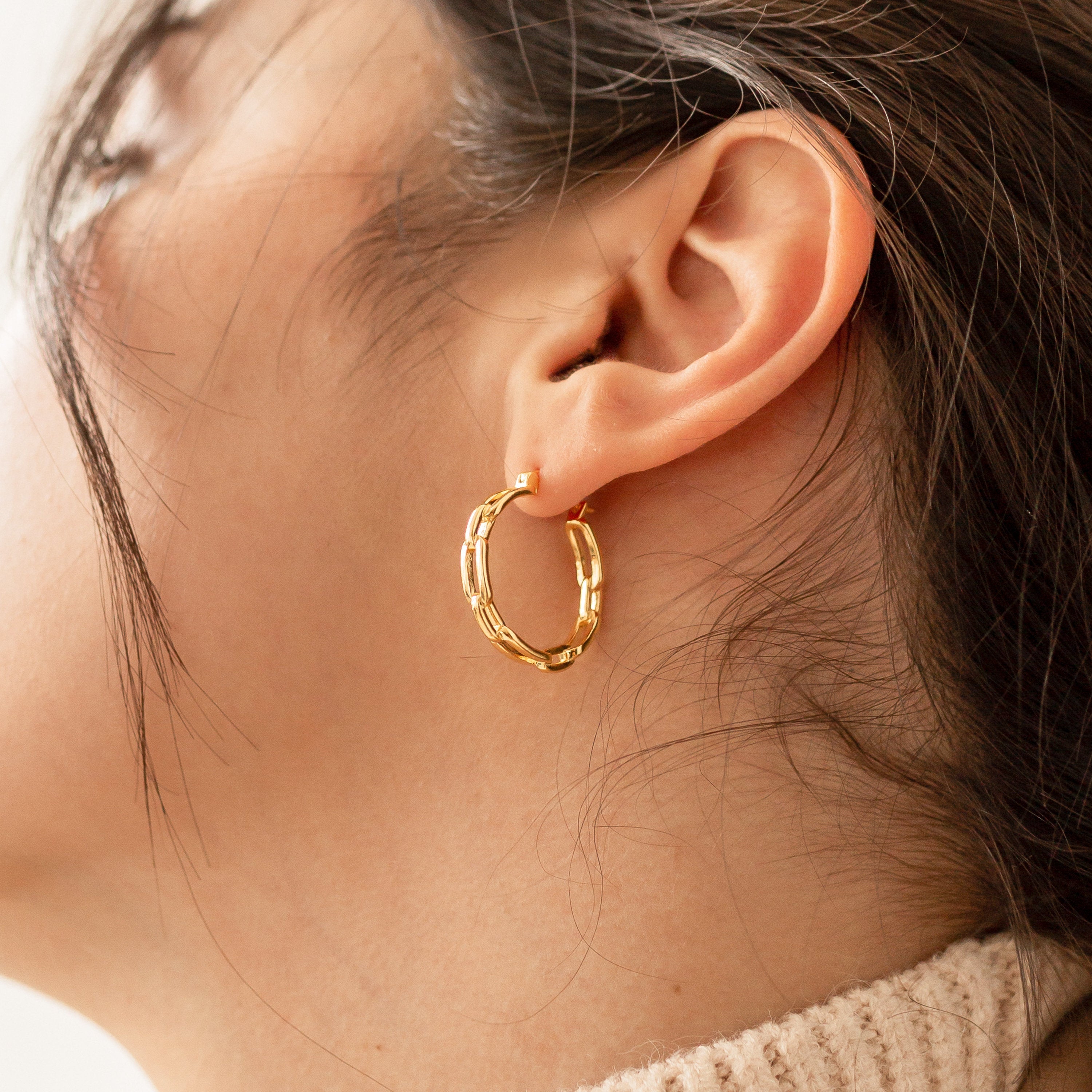 A close-up of a woman’s ear wearing Adele Link Hoops, modern statement gold earrings, with her hair partially covering her face.