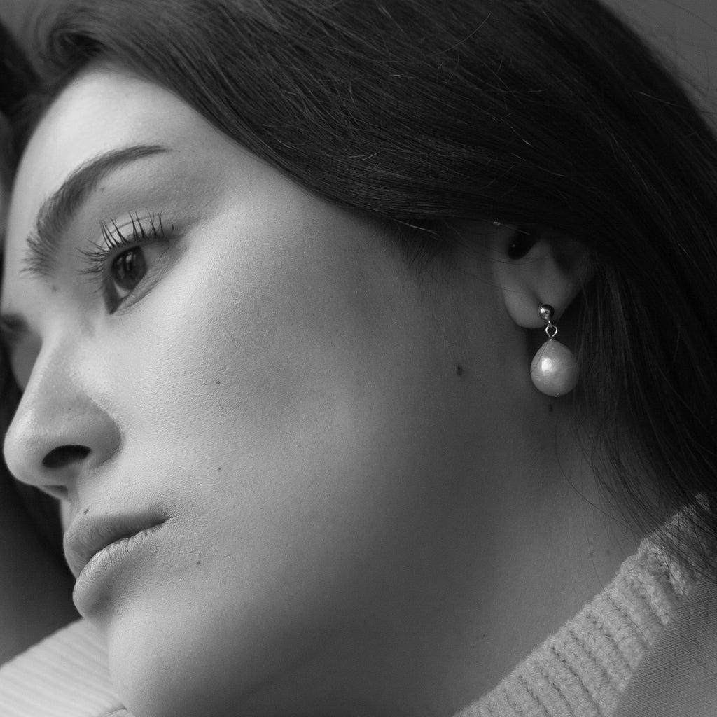 Black and white close-up of a woman lying down, wearing Baroque Pearl Earrings, gazing thoughtfully to the side.