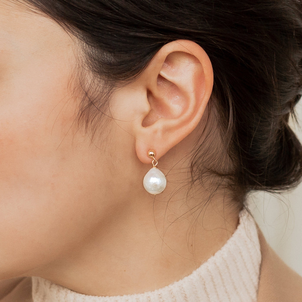 A close-up showcases a woman's ear adorned with Baroque Pearl Earrings, styled with dark hair and a beige turtleneck.