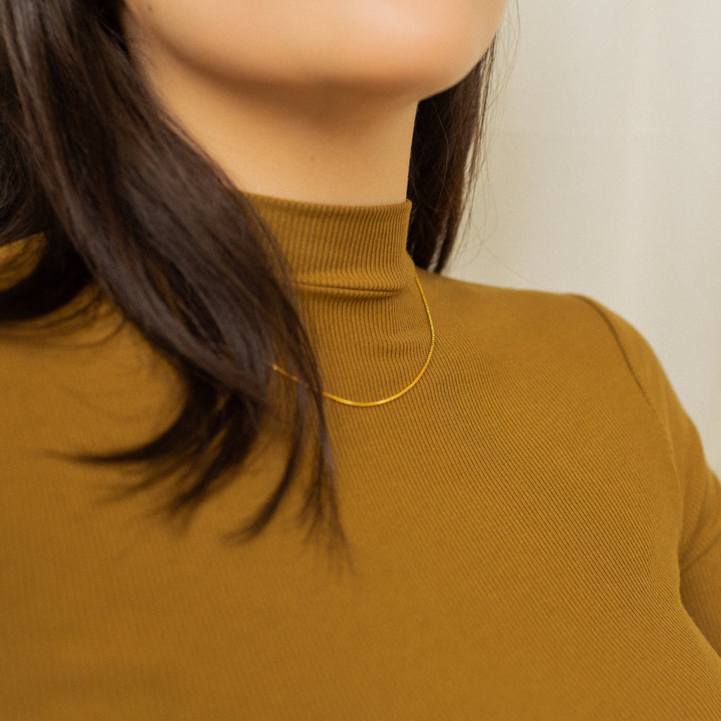 A front view of a gold box chain necklace worn with a mustard ribbed turtleneck