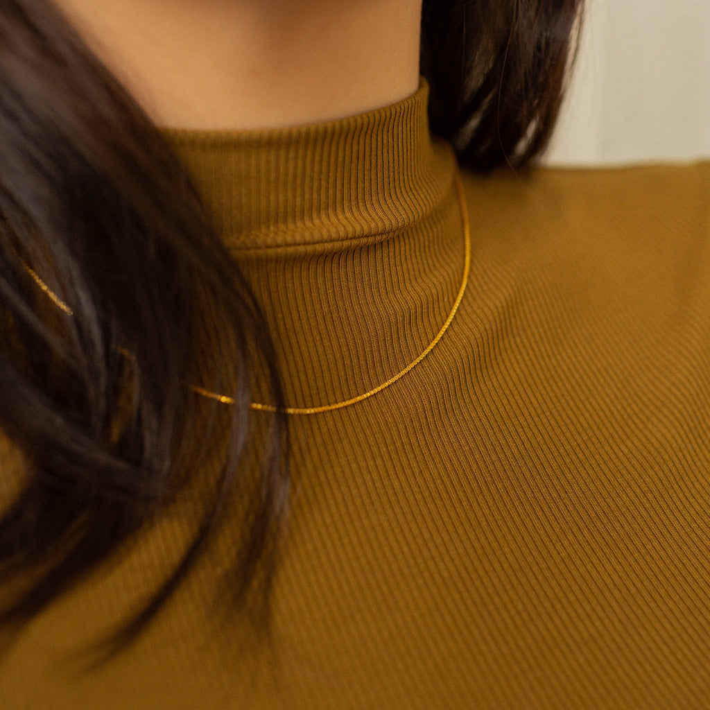 A gold box chain necklace styled over a model's neck