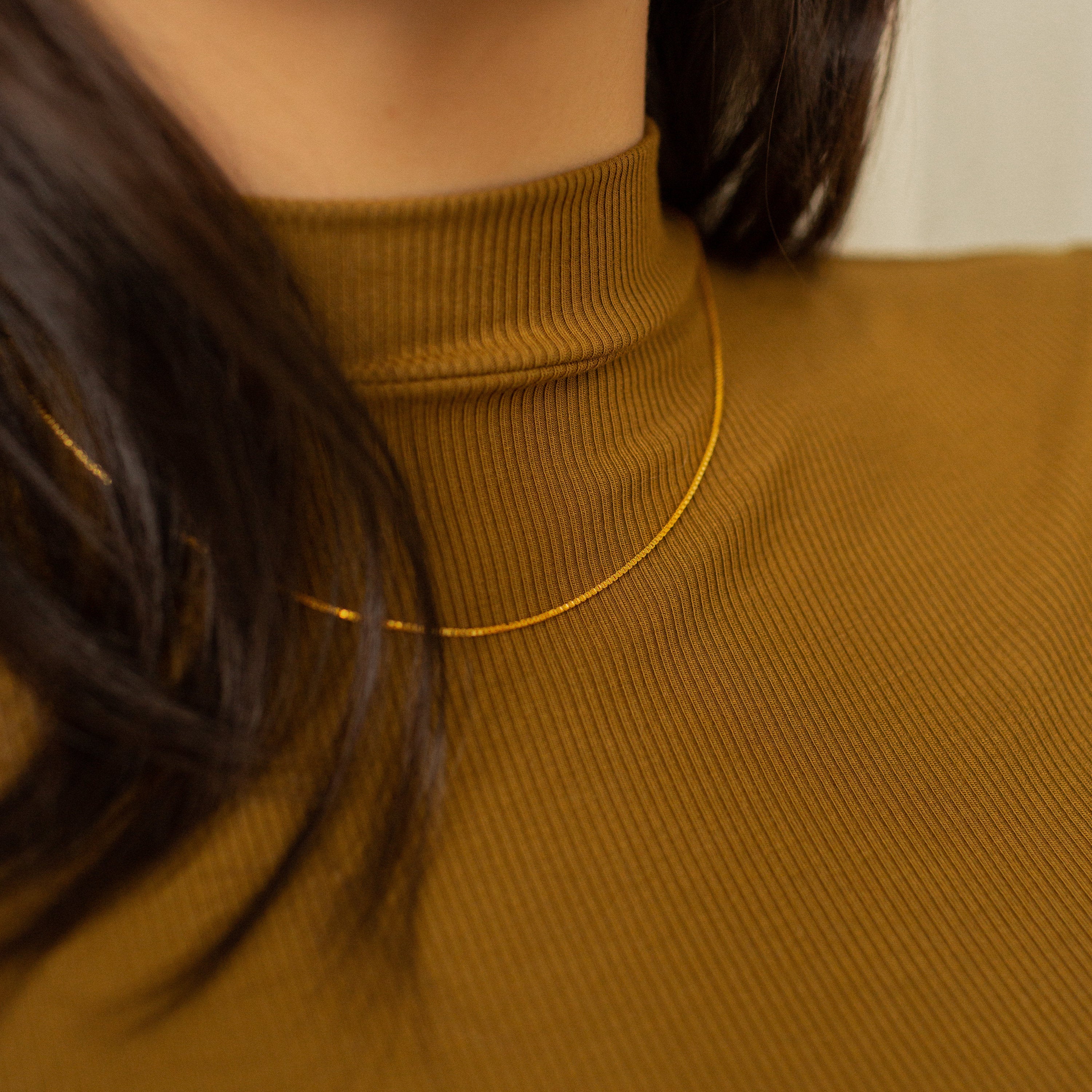 A gold box chain necklace styled over a model's neck