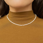 A close-up of a woman wearing the Pearl Choker Necklace paired with a brown ribbed turtleneck top.