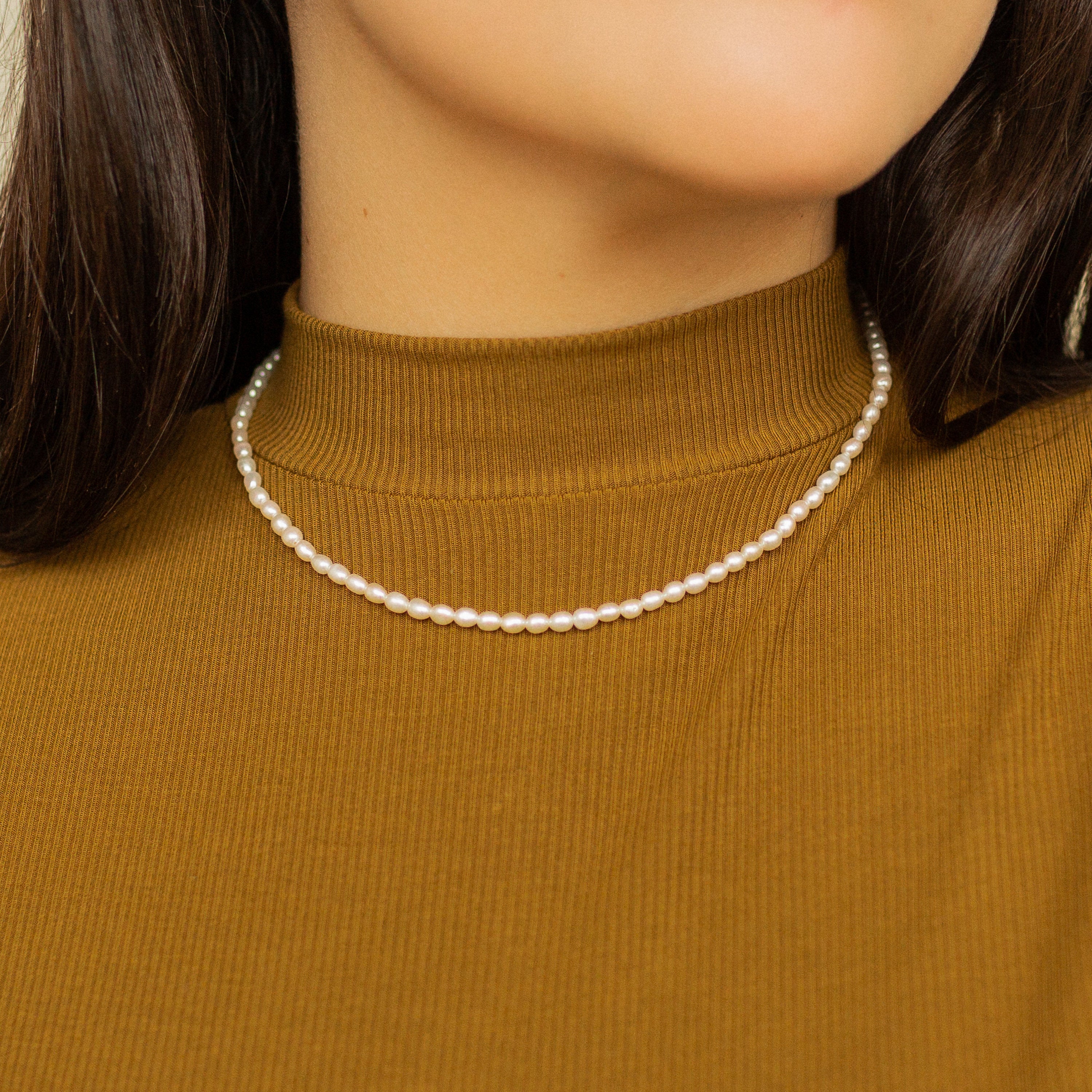 Woman wearing a Pearl Choker Necklace paired with a brown ribbed high-neck top.
