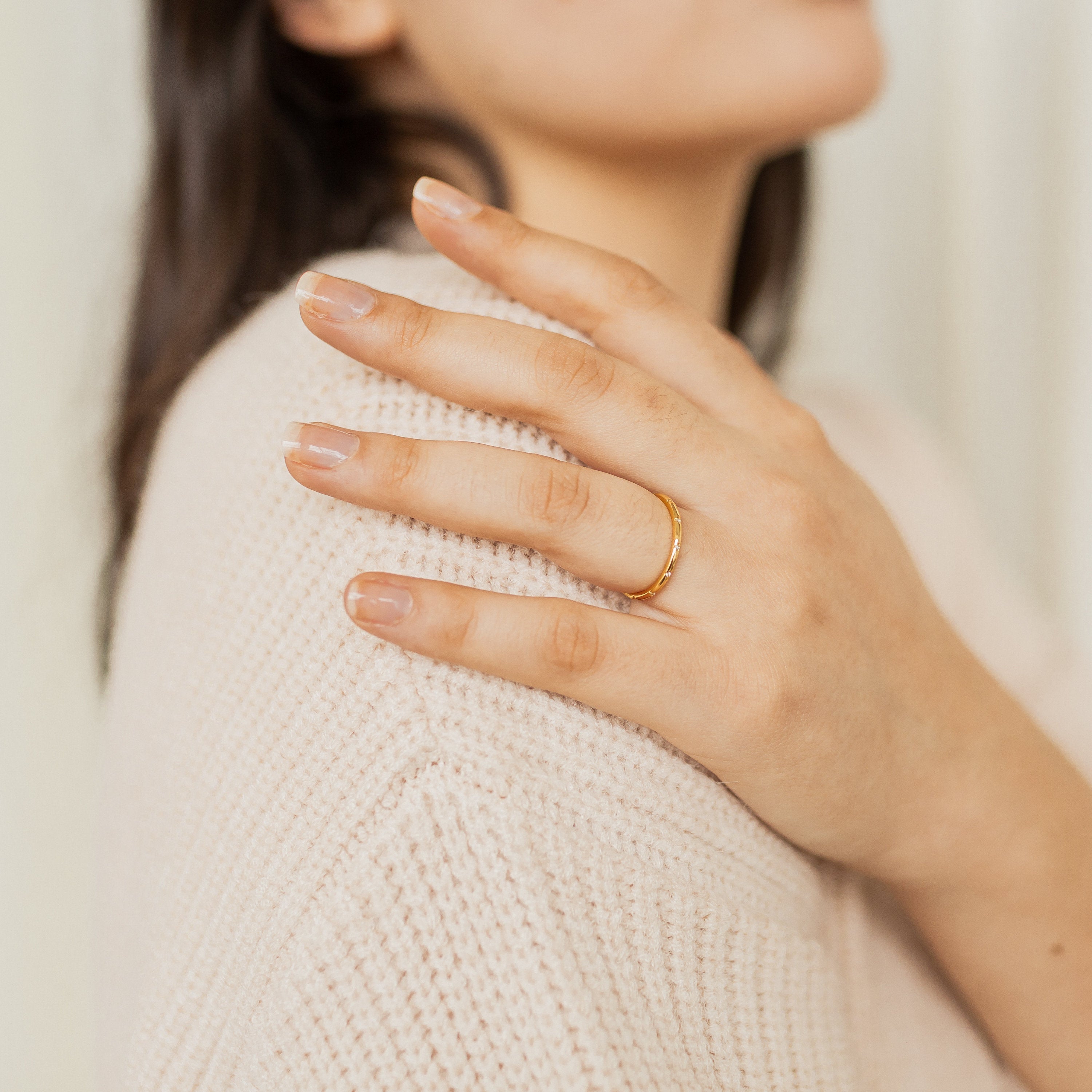 A woman wearing the Sprinkle Diamond Ring rests her hand on her shoulder, dressed in a cream knit sweater.