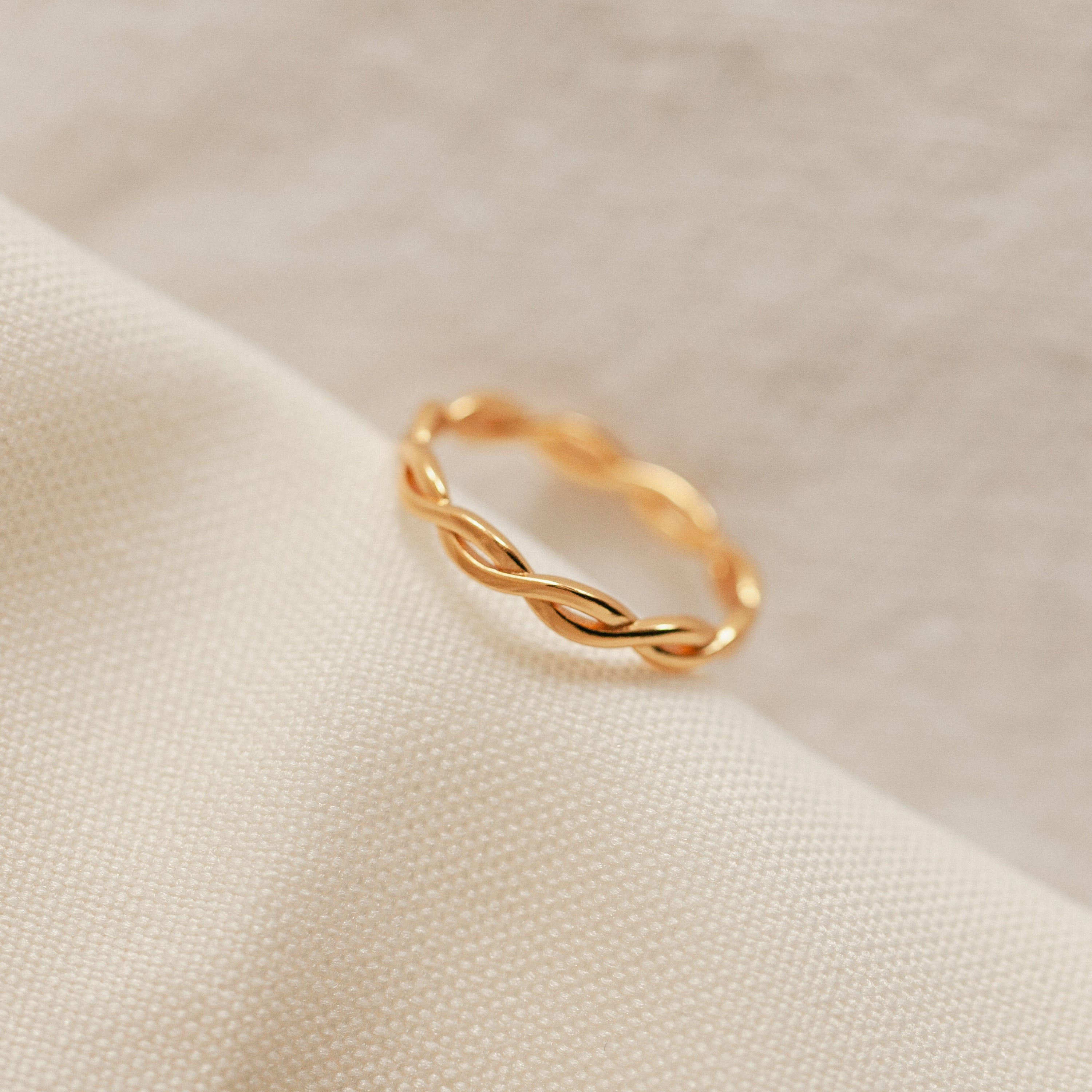 The Braided Ring shines elegantly on a white cloth, ideal for stacking or pairing with your favorite silver band.