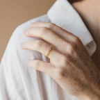 A freckled hand wears the Birthstone Curb Ring, featuring a small gemstone, resting on a white shirt.