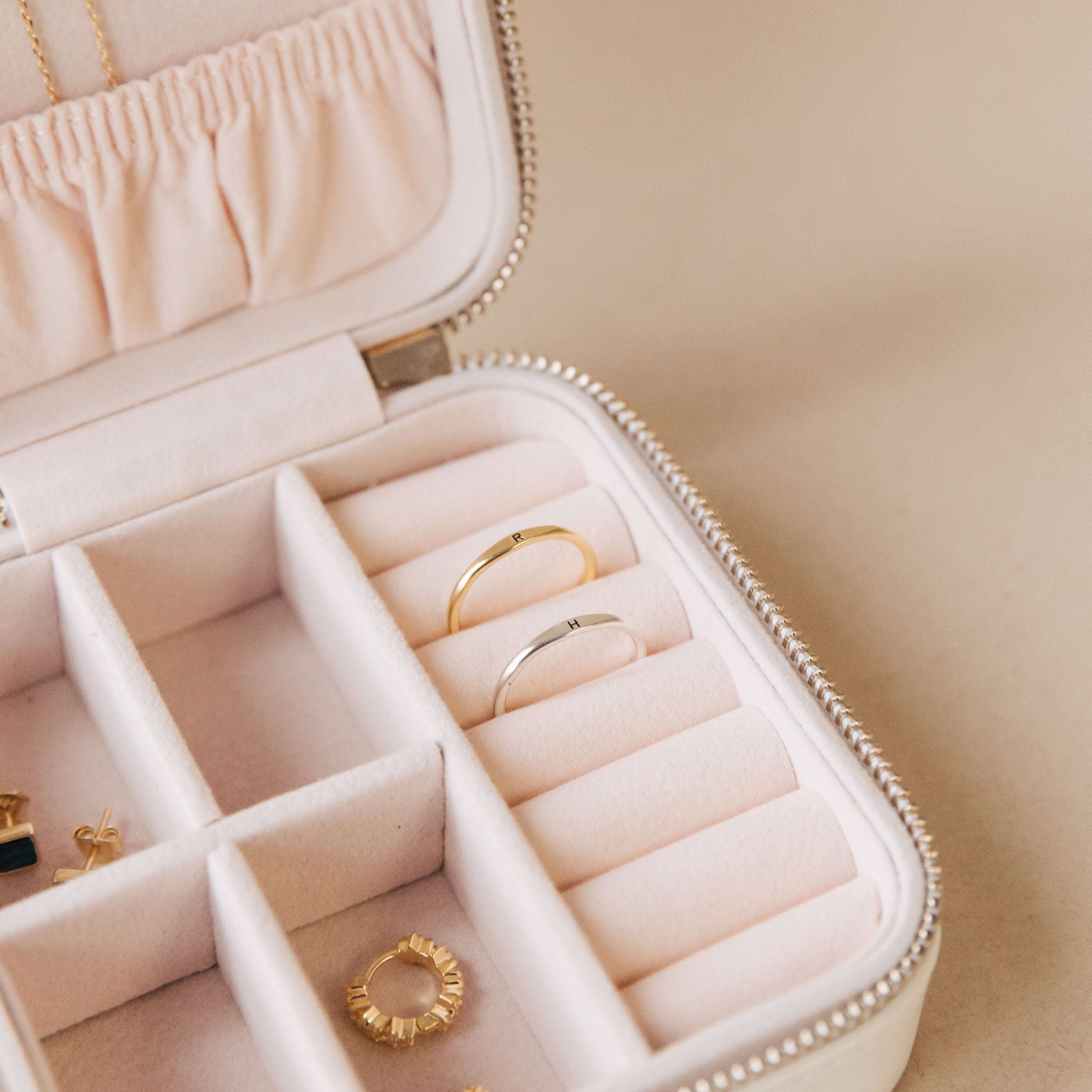 Open jewelry box with pink lining holds rings and earrings, including the Skinny Initial Ring and dainty stacking rings, each displayed in separate compartments.