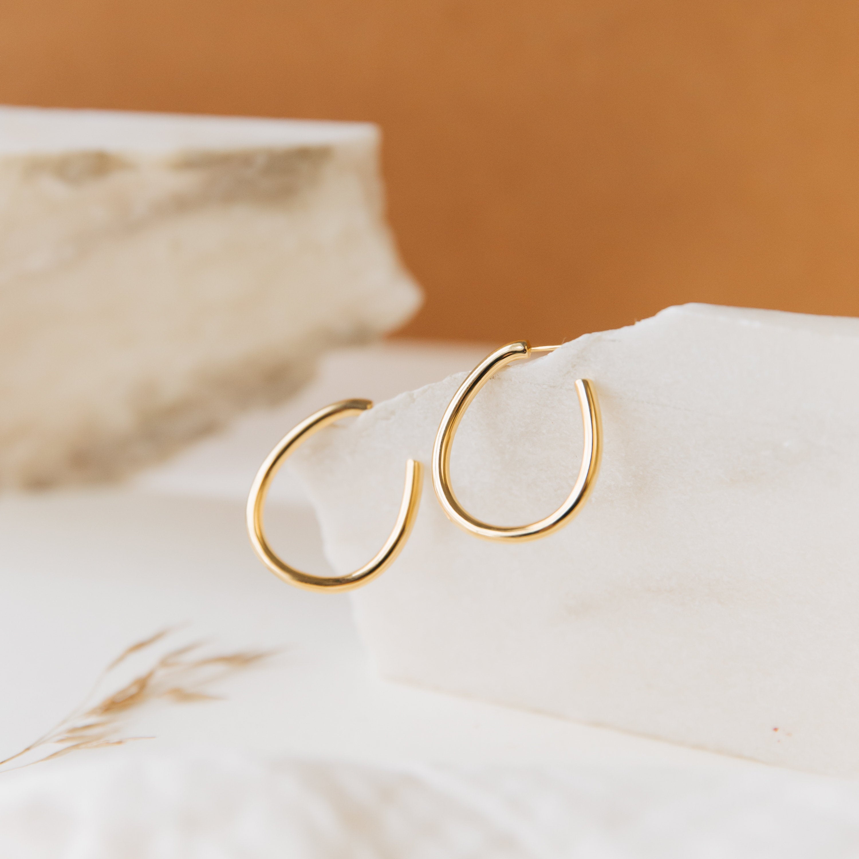 Anine Oval Hoops are displayed on a white stone with a beige background.