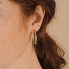 Close-up of a person with freckles and brown hair tied back, wearing Anine Oval Hoops.