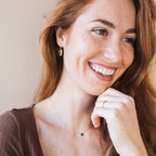 A woman smiling with her hand on her chin, highlighted by elegant Emerald Drop Earrings.