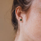 Close-up of a woman's ear wearing Malachite Studs—small, geometric box-shaped green earrings—with her freckles visible on her skin.