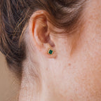 Close-up of a person's ear wearing Malachite Studs—geometric, box-shaped green earrings with a gold border.