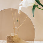 The Malachite Necklace is displayed on a textured stone slab with a white lily flower in the background.