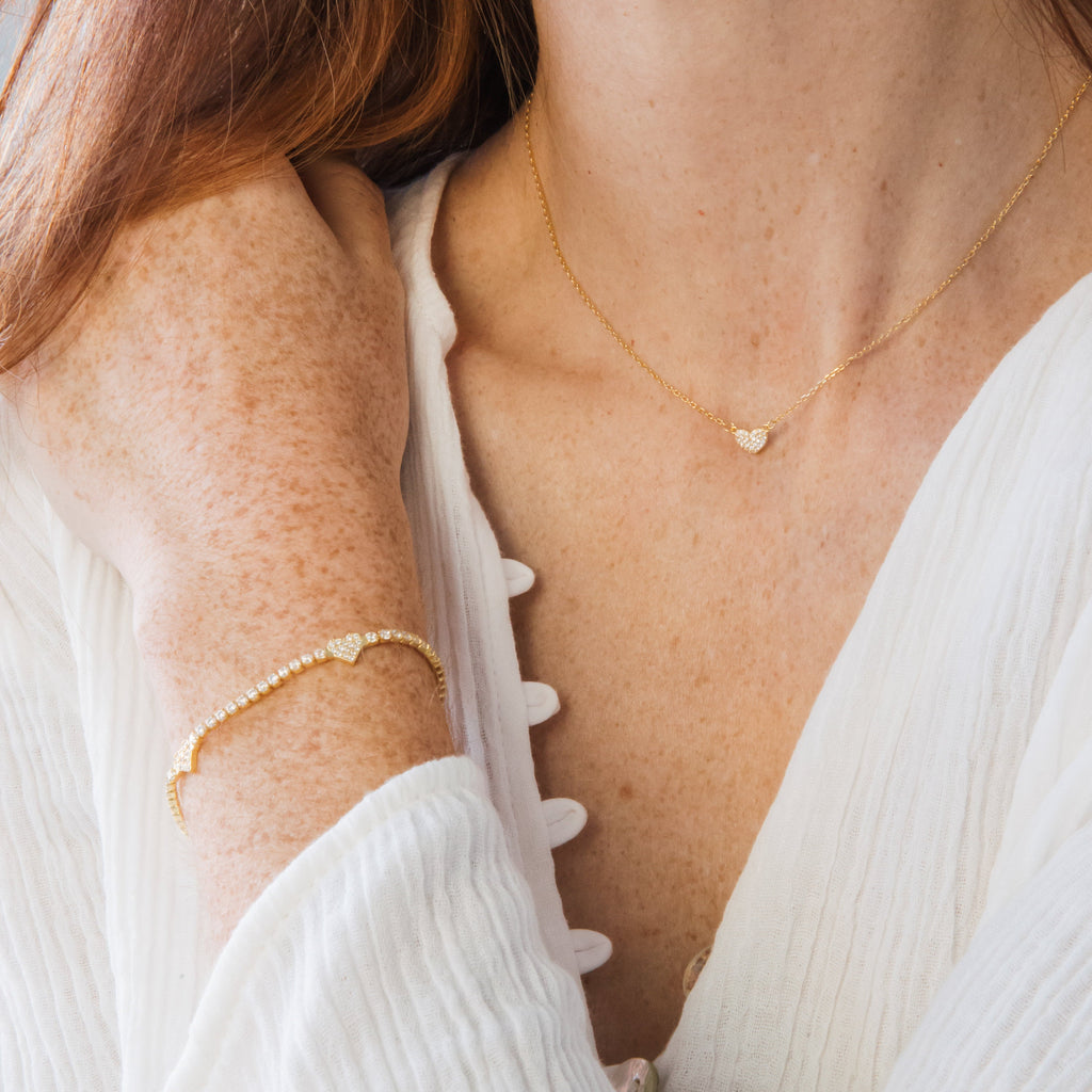 A woman wearing a gold tennis bracelet with pave hearts and the Pave Heart Necklace.