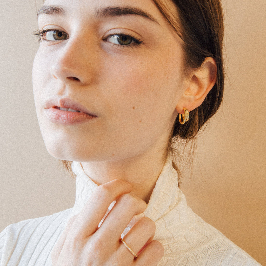 A woman with light skin wears a white turtleneck, gold ring, and Zoey Duo Hoops for a chic stacked ear look, gazing at the camera.
