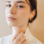 A woman with light skin wears a white turtleneck, gold ring, and Zoey Duo Hoops for a chic stacked ear look, gazing at the camera.