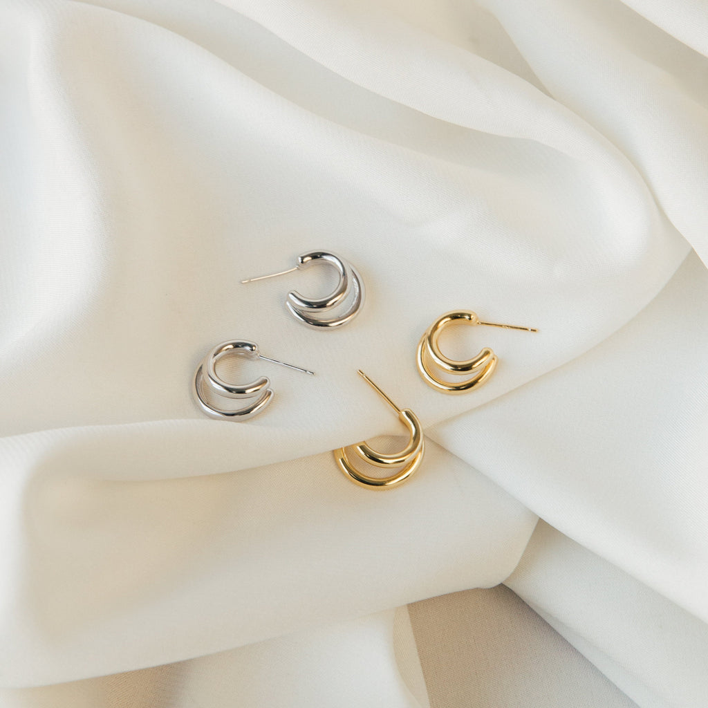 Two pairs of crescent-shaped Zoey Duo Hoops—one silver, one gold—displayed on white fabric; perfect for a chic stacked ear look.