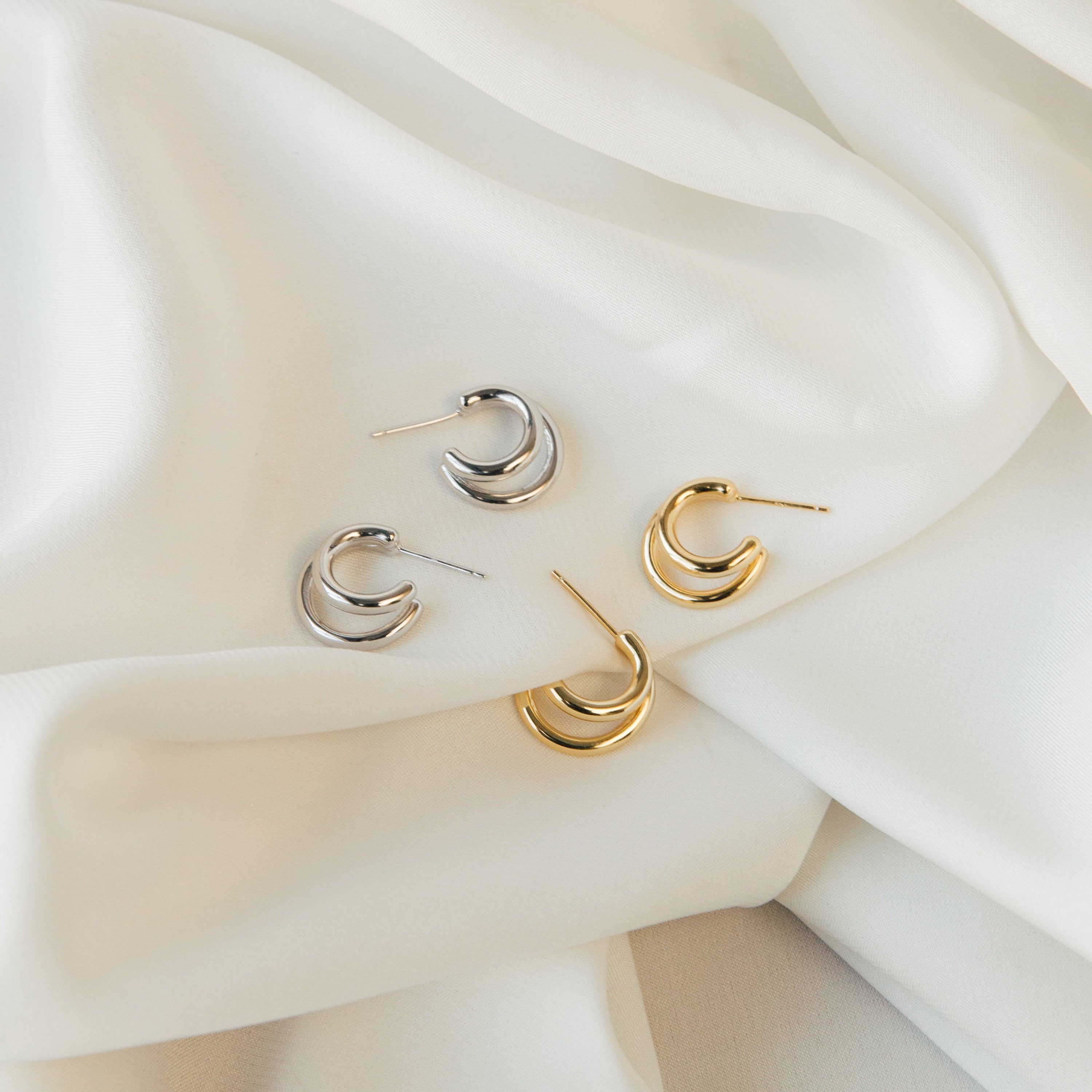 Two pairs of crescent-shaped Zoey Duo Hoops—one silver, one gold—displayed on white fabric; perfect for a chic stacked ear look.