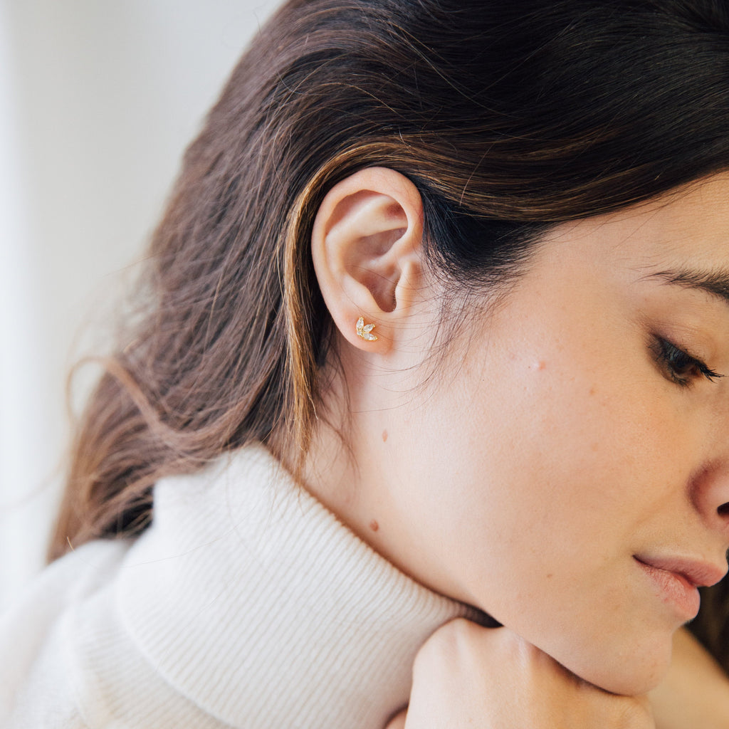 A woman with her hand on her chin exudes elegance, drawing attention to the sparkling Arya Petal Studs.