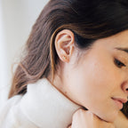 A woman with her hand on her chin exudes elegance, drawing attention to the sparkling Arya Petal Studs.