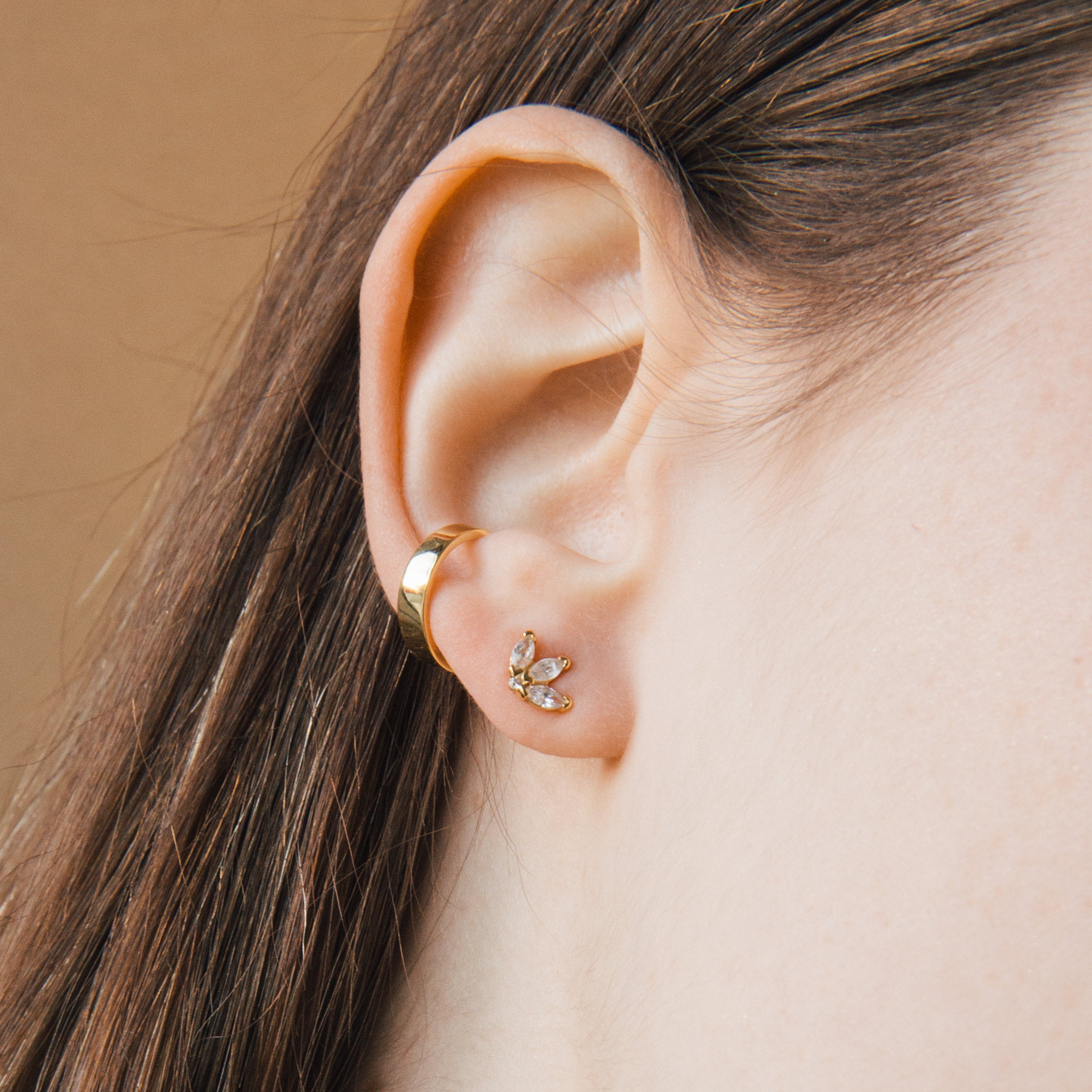 A close-up of an ear adorned with gold hoops and sparkling Arya Petal Studs, paired with a gold stud earring featuring small crystals.