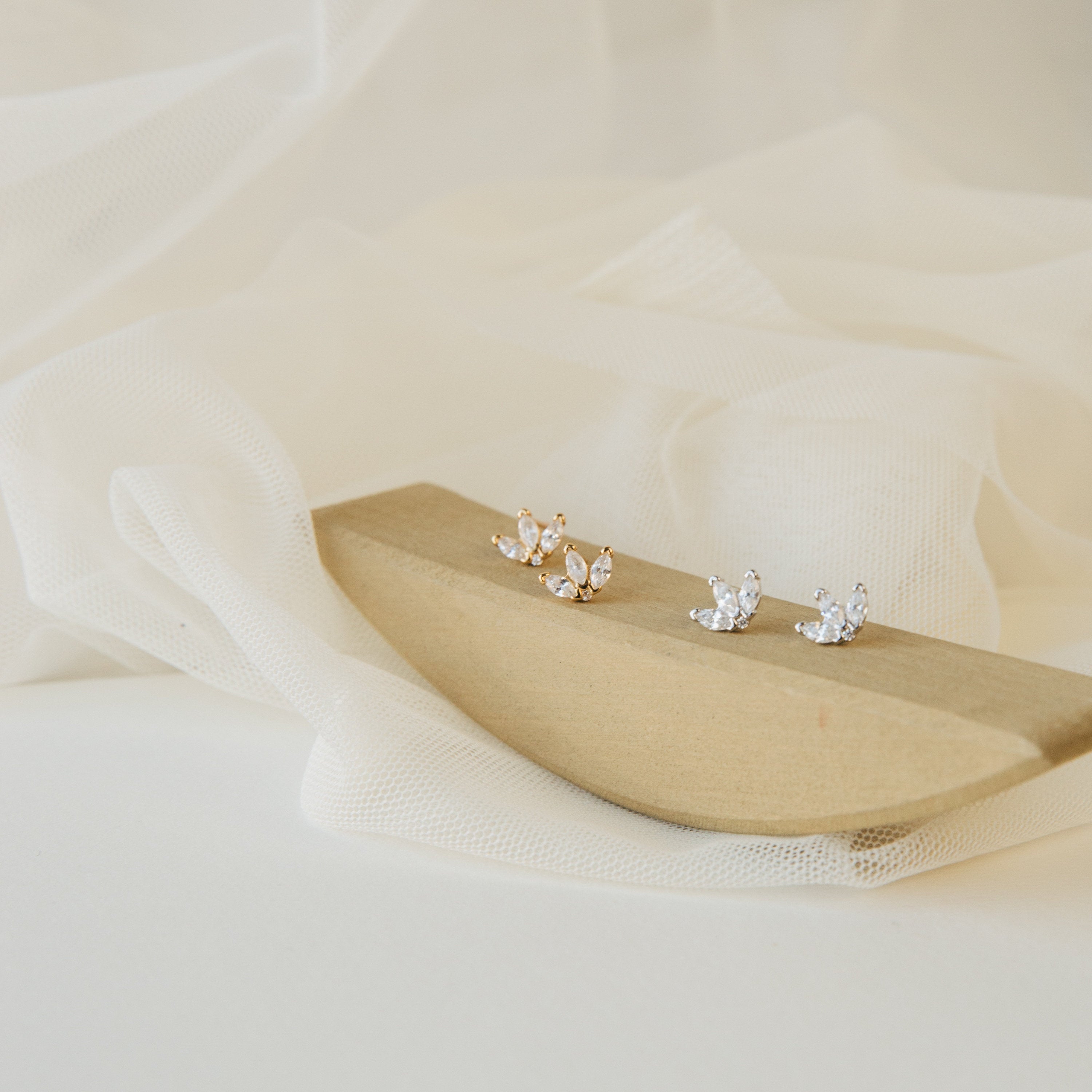 Arya Petal Studs in gold and silver are shown on a wooden holder with a white fabric background.
