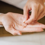 A person holds Stella Star Studs, small gold dainty earrings, in one hand and touches them with the other.