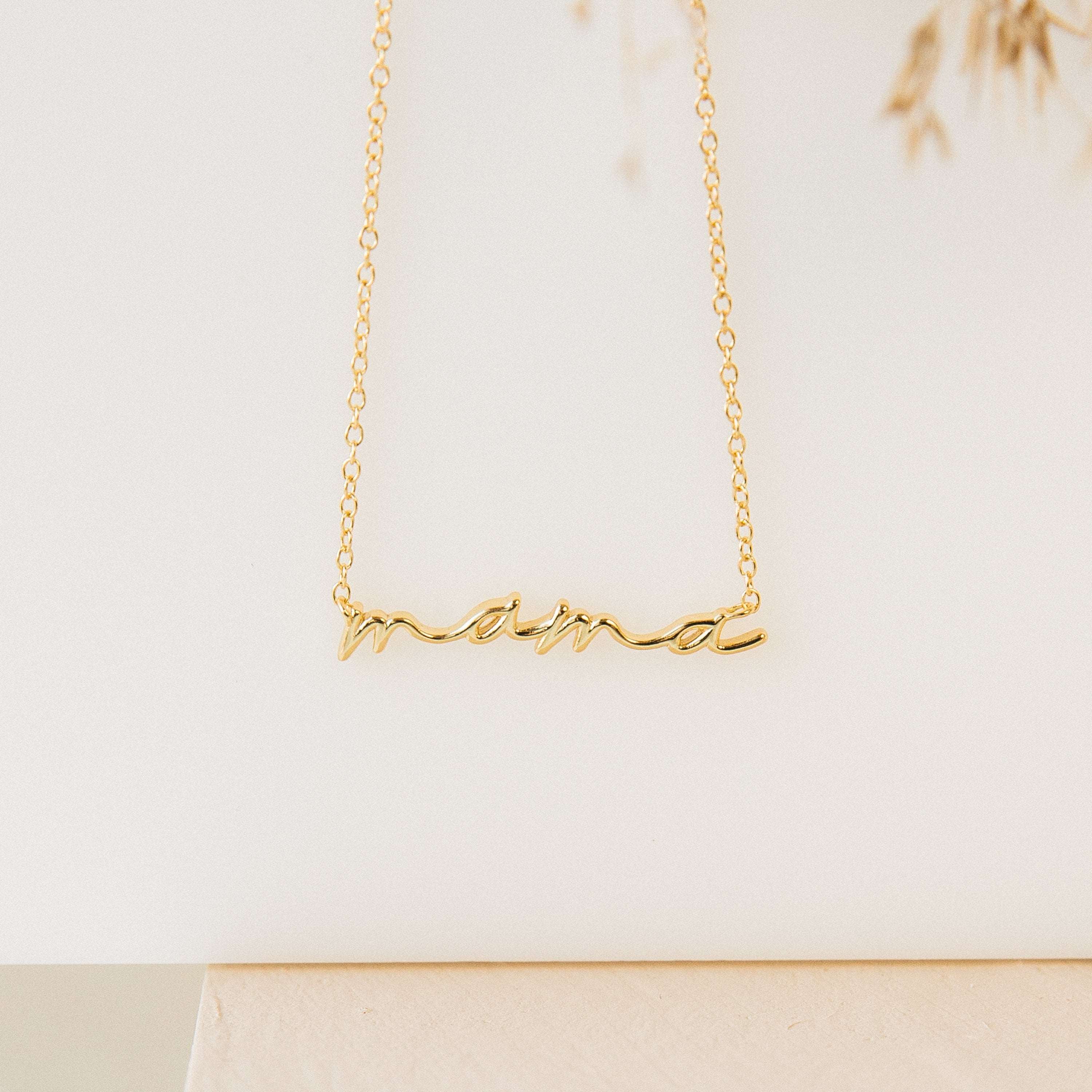 Gold necklace featuring the word “mama” in elegant cursive script, suspended from a delicate chain. Displayed against a clean, neutral background with soft lighting.