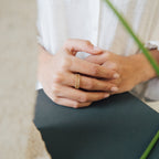 A person wearing a white shirt rests their hands, adorned with a Dove Eternity Ring, on a dark surface; a blurred plant appears in the foreground.