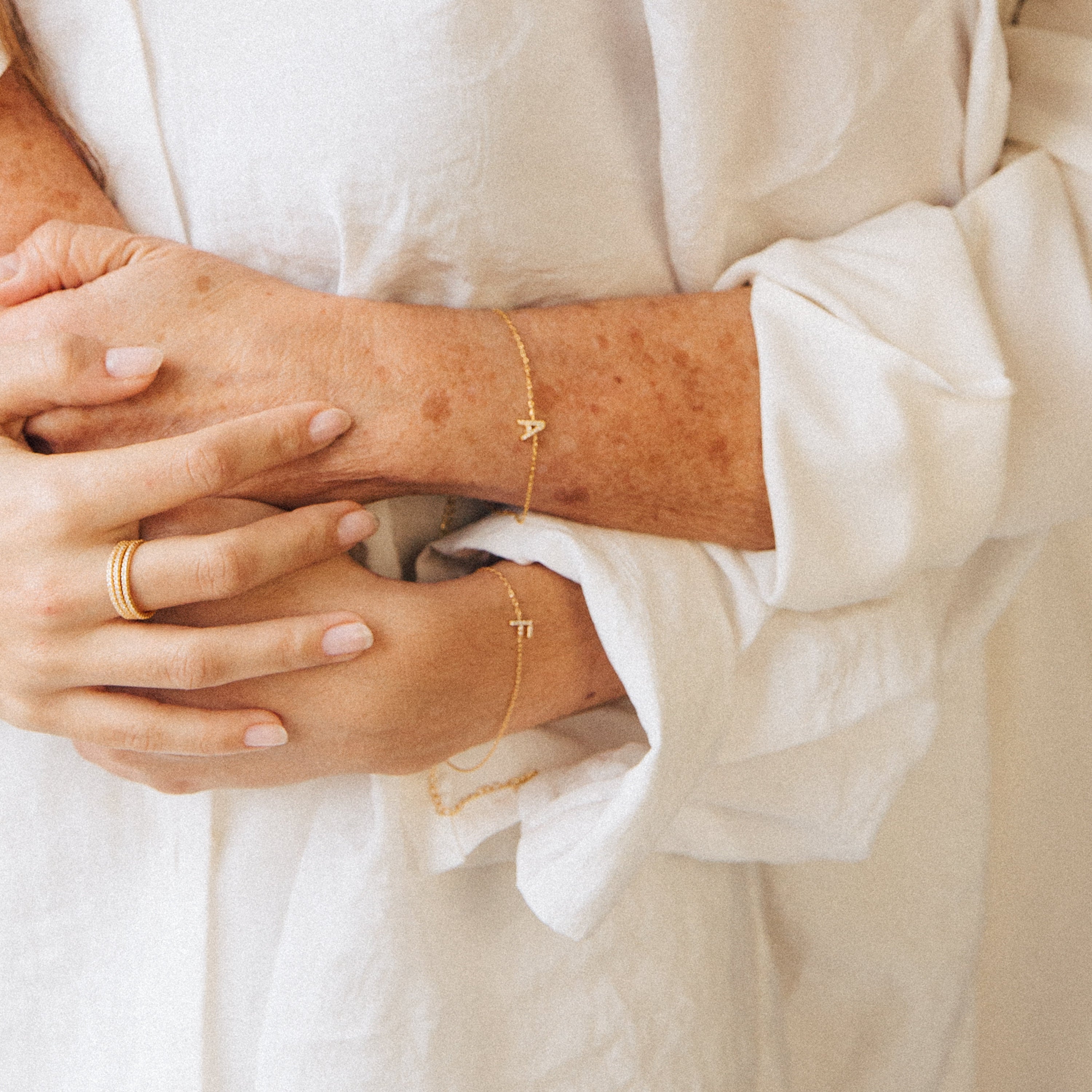 Close-up of two hands in a loose white long-sleeve shirt, wearing gold rings and the Pave Initial Bracelet.