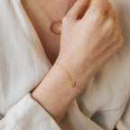 A person wears a gold necklace with a circle pendant and a Pave Initial Bracelet featuring an A charm.