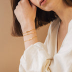 A woman in a white shirt highlights the Name Link Bracelet, a stylish piece of contemporary jewelry.