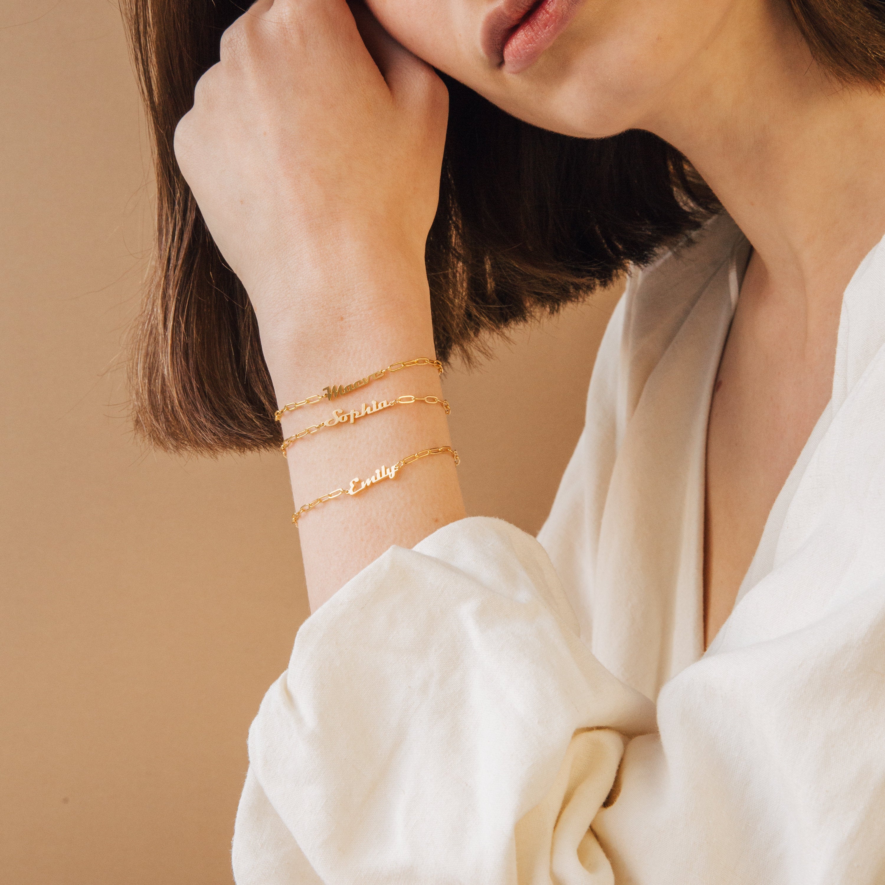 A woman in a white shirt highlights the Name Link Bracelet, a stylish piece of contemporary jewelry.