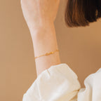 The Name Link Bracelet with "emily" rests on a wrist, highlighting elegant contemporary jewelry against a neutral beige background.