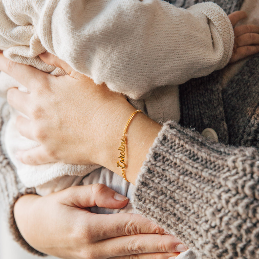 Close-up of an adult holding a baby, wearing the Ladybirds Name Curb Bracelet with a cursive name design.