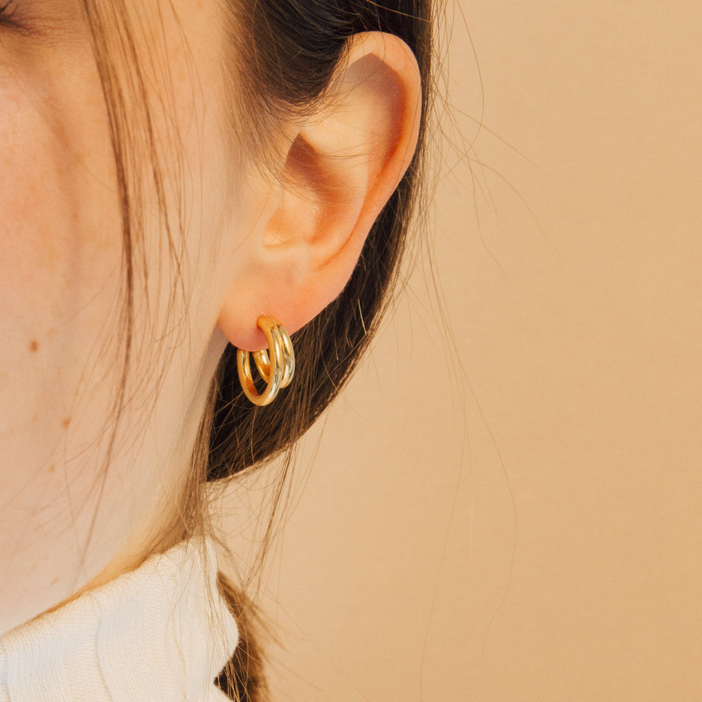 Close-up of a woman's ear wearing Zoey Duo Hoops, with brown hair and a cream-colored turtleneck—perfect for a chic, stacked ear look.
